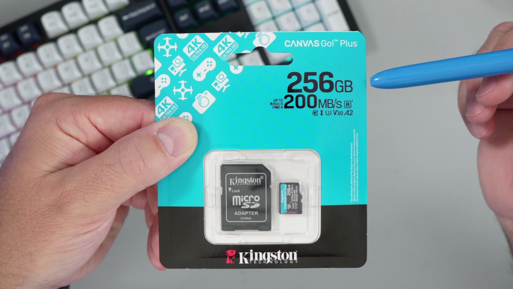 A hand holding the Kingston Canvas Go Plus 256GB microSD card in its retail packaging, with a stylus pointing to the 200MB/s speed rating on the front.