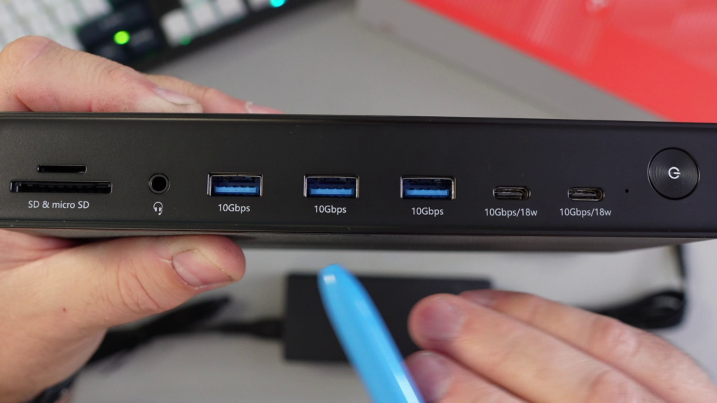 A close-up of the front panel of the TobenONE UDS050A docking station, showing SD/micro SD slots, audio jack, three 10Gbps USB-A ports, two 10Gbps/18W USB-C ports, and the power button, with a blue pen pointing to the USB ports.