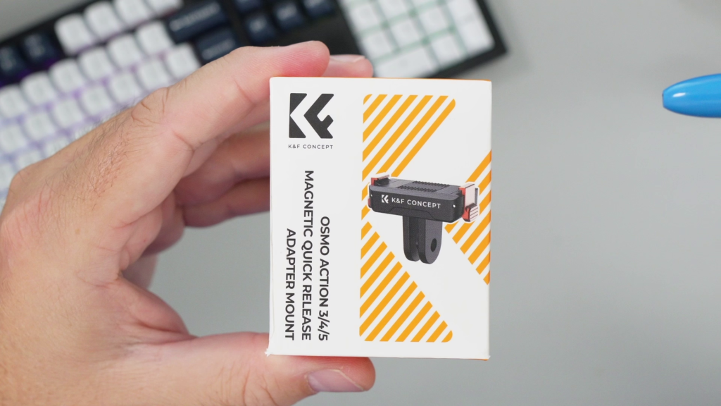 A hand holding the small white retail box for the K&F Concept Magnetic Quick Release Adapter Mount, designed for DJI Osmo Action 3/4/5 cameras, with an image of the mount.
