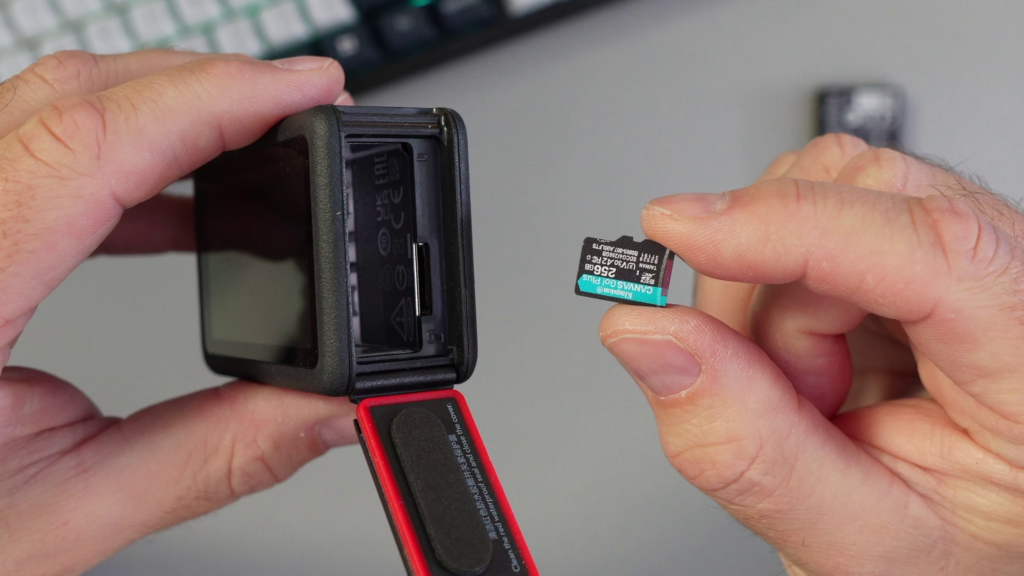 A hand holding a 256GB Kingston Canvas Go! Plus microSD card next to the open battery slot of the DJI Osmo Action 6 camera.