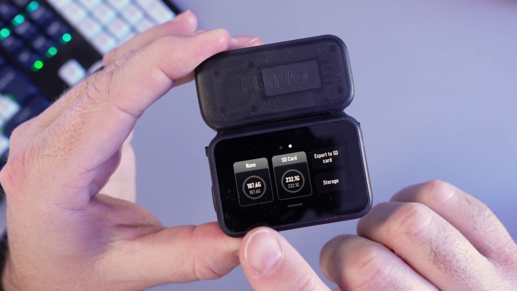 A person holding the DJI Osmo Nano Vision Dock, showing the touch screen interface with 107.6GB of internal storage and 232.1GB of microSD card space available for export.